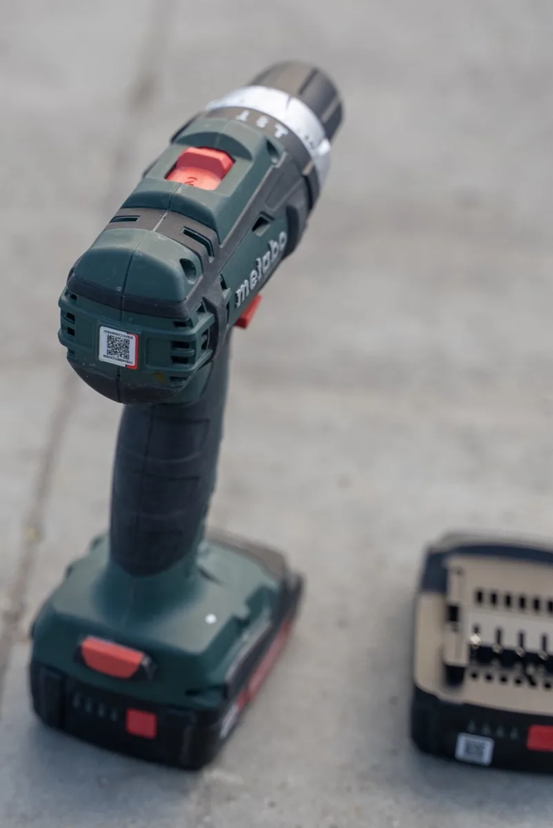 A Metabo cordless drill on concrete with an ItemRecover QR sticker on the battery